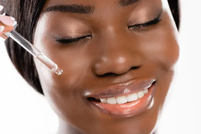 How to prevent acne before period: Black woman applying a face serum | Niacinamid helps regulate sebum production, and helps prevent period pimples and break outs.