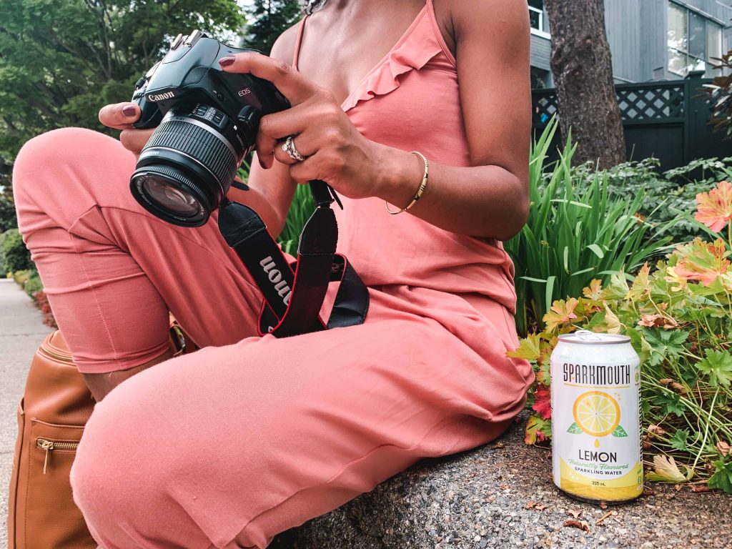 Black Canadian Blogger, Comfy Girl with Curls reviewing photos on camera. SPARKMOUTH Sparkling Water in lemon. (Close Up). Find Your Spark.