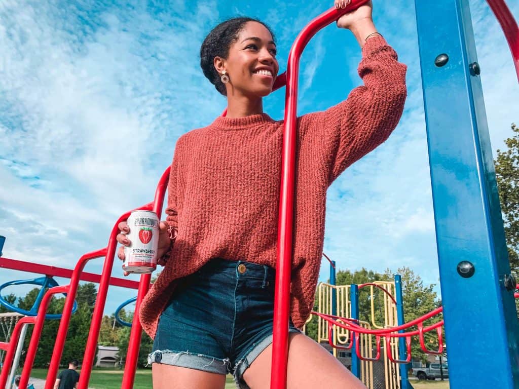 Comfy Girl with Curls holding Sparkmouth sparkling water in Strawberry flavour. Canadian, BC brand. Find My Spark.