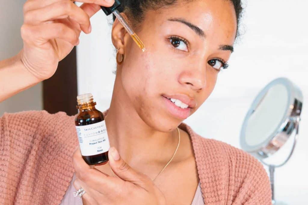 Black Canadian Blogger with hyperpigmentation concerns applying personalized skincare, Custom DOSE, with eye dropper/pipette.