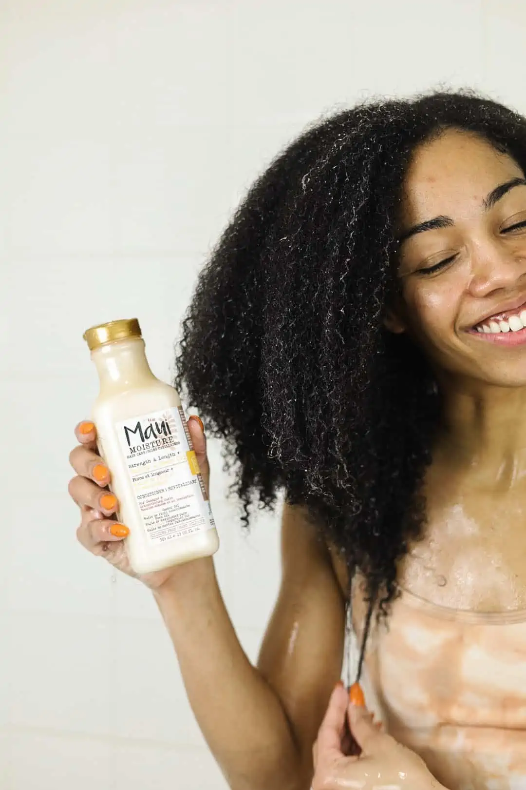 Holding Maui Moisture Conditioner in shower while stretching natural hair to show length.