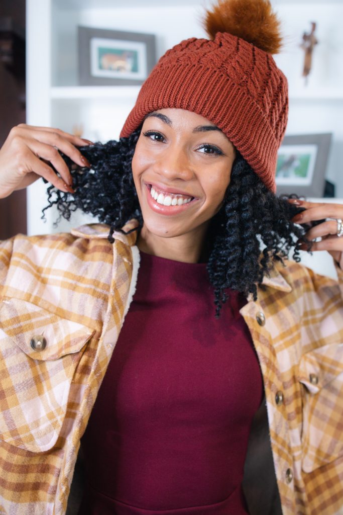 Black Girl Blogger ComfyGirlCurls wearing a lumberjack shacket and burnt orange beanie holding natural hair styled in twist out.