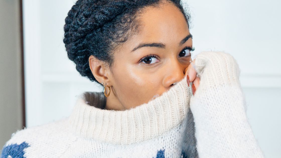 Black Girl with hair in protective style (medium-sized twists) wearing thick wool winter sweater over face.